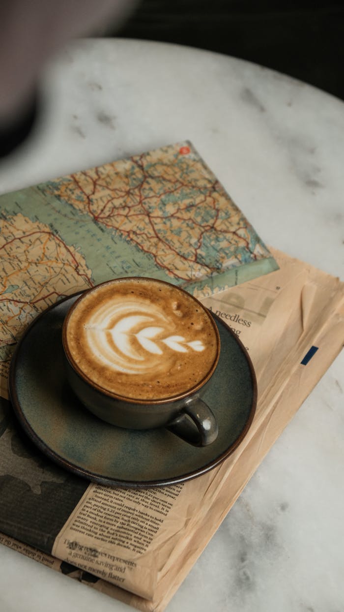 Artistic cappuccino on newspapers and a map, perfect for travel inspiration.
